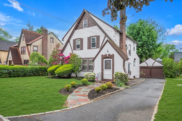 tudor home featuring a detached garage, a front yard, an outbuilding, and a chimney