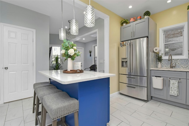 kitchen featuring stainless steel refrigerator with ice dispenser, a sink, light marble finish floors, a kitchen breakfast bar, and light countertops
