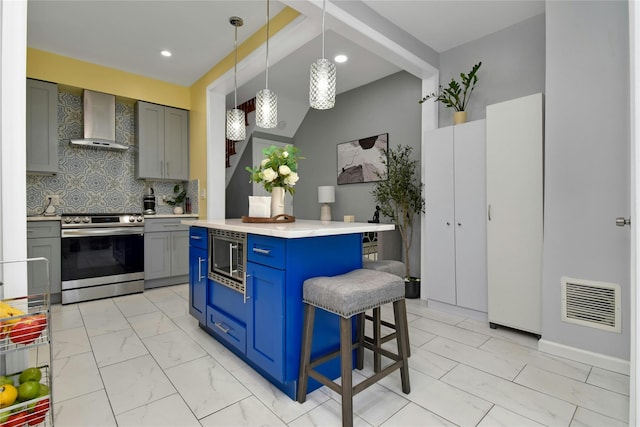 kitchen featuring stainless steel appliances, wall chimney exhaust hood, a breakfast bar area, tasteful backsplash, and light countertops