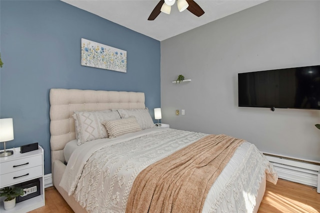 bedroom featuring light wood-style floors, a ceiling fan, and a baseboard radiator