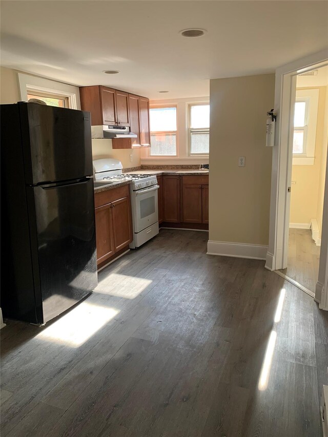 kitchen featuring freestanding refrigerator, white range with gas cooktop, under cabinet range hood, dark wood-type flooring, and brown cabinets