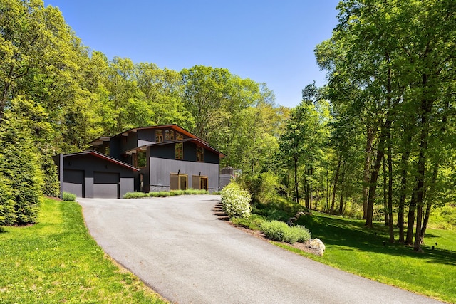 view of front of home featuring an outbuilding, a front lawn, a wooded view, and asphalt driveway