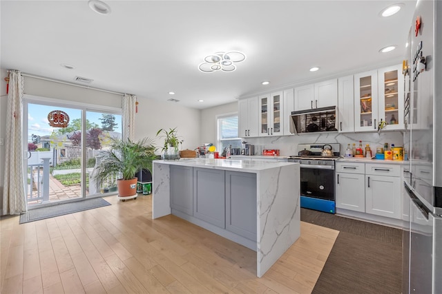3875 S St, Seaford, NY 11783 - kitchen with stainless steel range with gas cooktop, white cabinets, a kitchen island, recessed lighting, and light stone countertops
