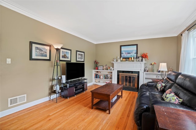 living room featuring light wood-type flooring, crown molding, baseboards, and a glass covered fireplace