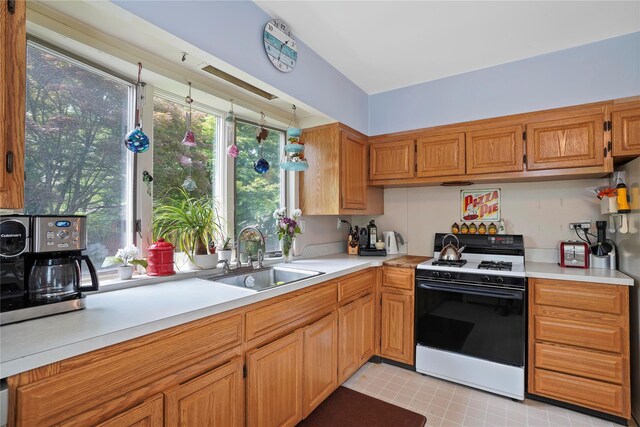 kitchen featuring white range with gas cooktop, a sink, light countertops, and brown cabinetry