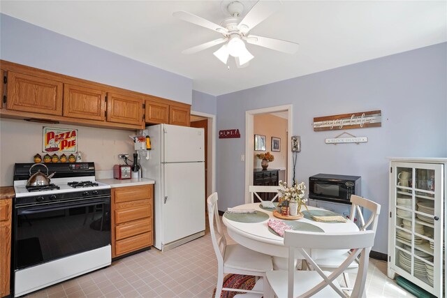kitchen featuring gas range oven, freestanding refrigerator, light countertops, ceiling fan, and black microwave