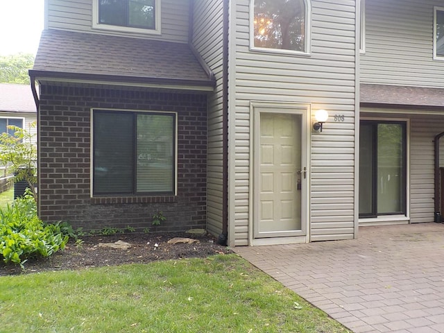 808 Woodland Ct, Coram, NY 11727 - property entrance featuring brick siding, a shingled roof, a patio area, and a yard