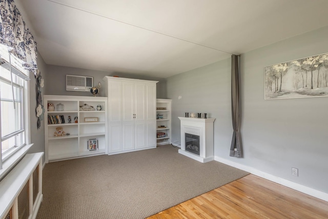 251-12 71st Rd Unit 29B, Bellerose, NY 11426 - unfurnished living room featuring a glass covered fireplace, light wood-style floors, baseboards, and an AC wall unit