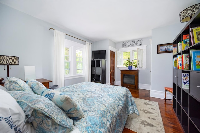 bedroom featuring wood finished floors, baseboards, and a glass covered fireplace