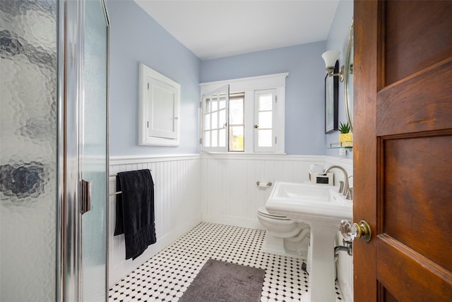 full bathroom featuring a wainscoted wall, a stall shower, toilet, and a sink
