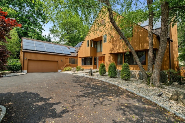 5 Ponds Ln, Purchase, NY 10577 - view of front of home featuring an attached garage, roof mounted solar panels, and asphalt driveway