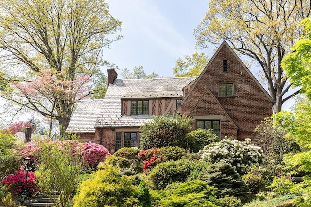 tudor-style house with a high end roof, a chimney, and brick siding