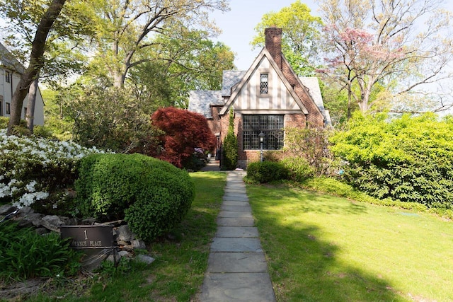 view of front facade with a front yard, a chimney, and brick siding