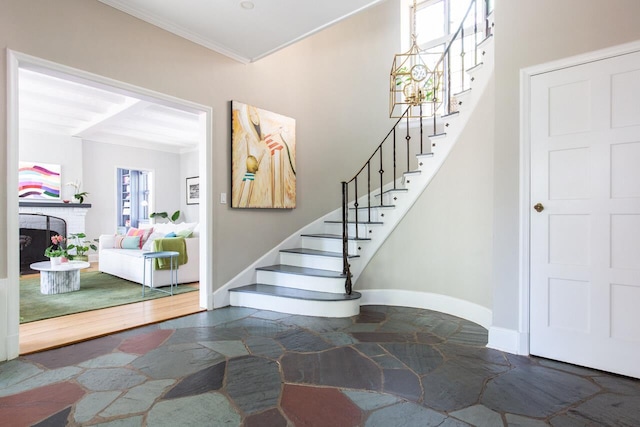 entryway featuring stone flooring, stairs, ornamental molding, a fireplace, and baseboards