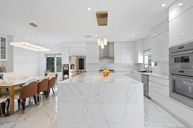 kitchen with appliances with stainless steel finishes, modern cabinets, wall chimney range hood, a sink, and light marble finish floors