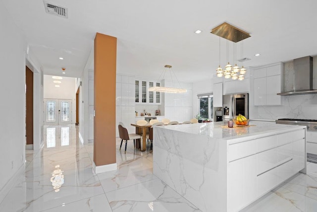 kitchen featuring wall chimney exhaust hood, stainless steel refrigerator with ice dispenser, modern cabinets, light marble finish floors, and recessed lighting