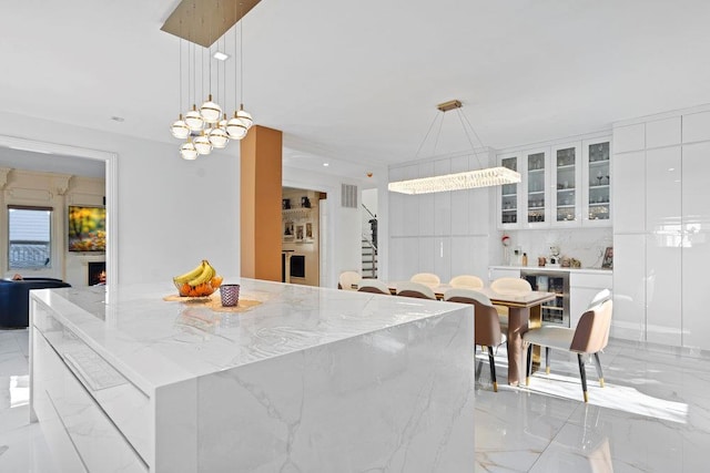 kitchen featuring light marble finish floors, white cabinets, light stone countertops, modern cabinets, and a chandelier