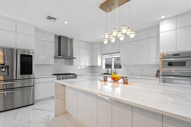 kitchen featuring appliances with stainless steel finishes, wall chimney range hood, modern cabinets, light marble finish floors, and recessed lighting