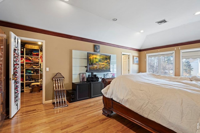 bedroom featuring a spacious closet, light wood-style floors, lofted ceiling, a closet, and ornamental molding