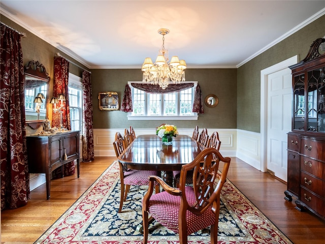 dining room with a chandelier, plenty of natural light, wood finished floors, wainscoting, and crown molding