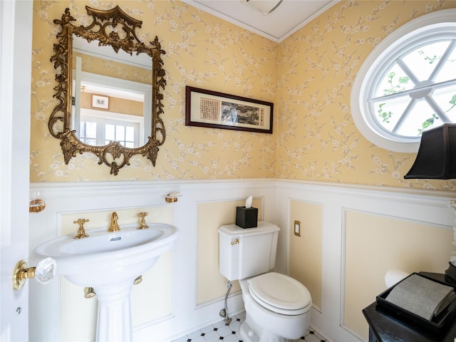 half bathroom featuring a wainscoted wall, plenty of natural light, toilet, and wallpapered walls