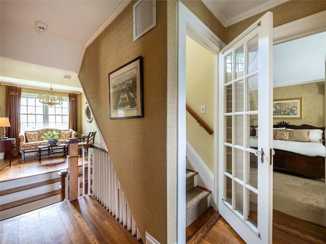 staircase with crown molding, wood-type flooring, a chandelier, french doors, and wallpapered walls