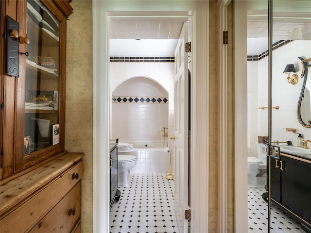 bathroom featuring toilet, vanity, tiled tub, and wallpapered walls