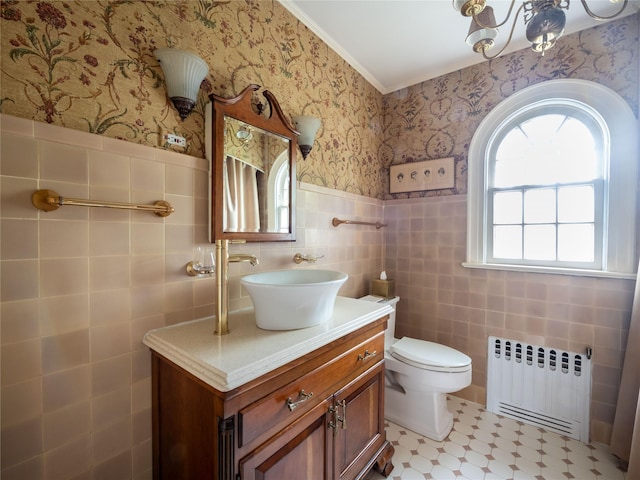 half bathroom with radiator heating unit, ornamental molding, wallpapered walls, vanity, and wainscoting