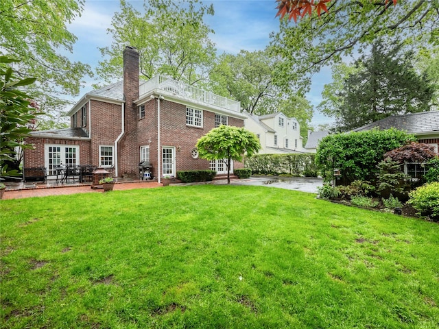 rear view of house with a chimney, a lawn, a patio area, brick siding, and french doors