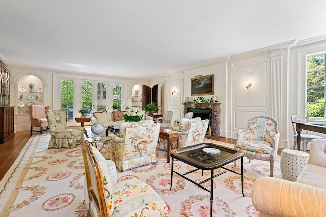 living area with wood finished floors, a fireplace, built in shelves, and ornamental molding