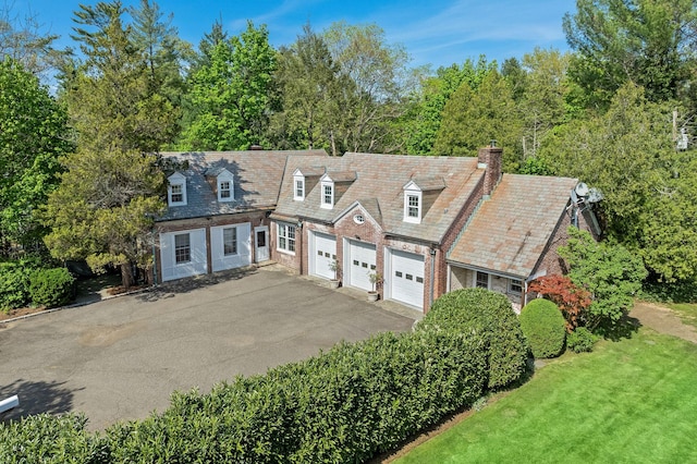 cape cod-style house with asphalt driveway, a garage, a chimney, and a front lawn