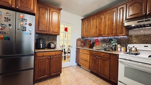 kitchen with freestanding refrigerator, white gas range oven, extractor fan, decorative backsplash, and a sink