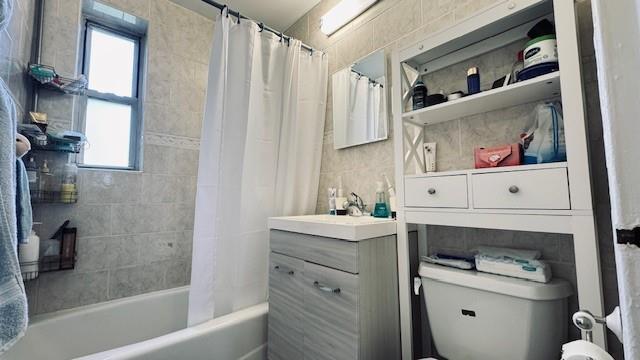 bathroom featuring shower / bath combo with shower curtain, toilet, vanity, and tile walls