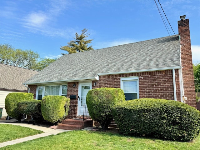 view of front facade with roof with shingles, a chimney, and brick siding