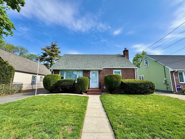 view of front of property with brick siding, a front lawn, a chimney, and roof with shingles