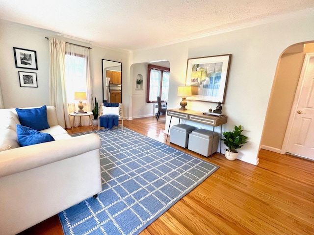 living room with arched walkways, wood finished floors, ornamental molding, baseboards, and a textured ceiling