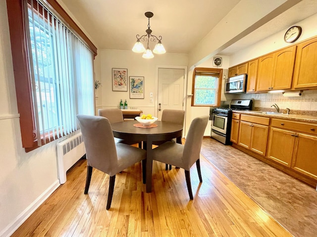dining room with radiator heating unit, light wood-type flooring, a chandelier, and baseboards