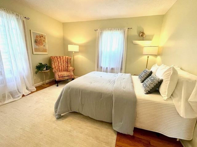 bedroom with multiple windows, wood finished floors, and baseboards
