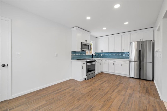 121 Arlington Ave, Wyandanch, NY 11798 - kitchen featuring stainless steel appliances, backsplash, light countertops, wood finished floors, and white cabinetry