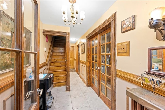 corridor featuring a chandelier, french doors, stairs, light tile patterned flooring, and wainscoting