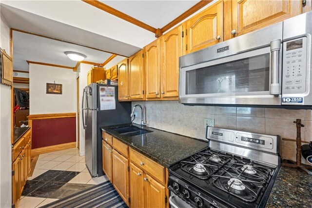 kitchen with appliances with stainless steel finishes, crown molding, a sink, dark stone counters, and tasteful backsplash