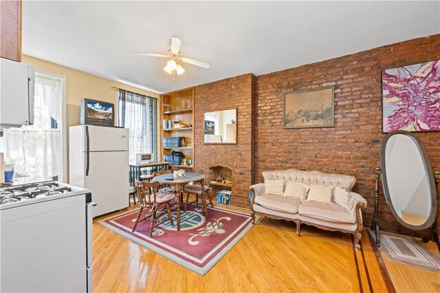 living area with a ceiling fan, brick wall, wood finished floors, built in shelves, and a fireplace