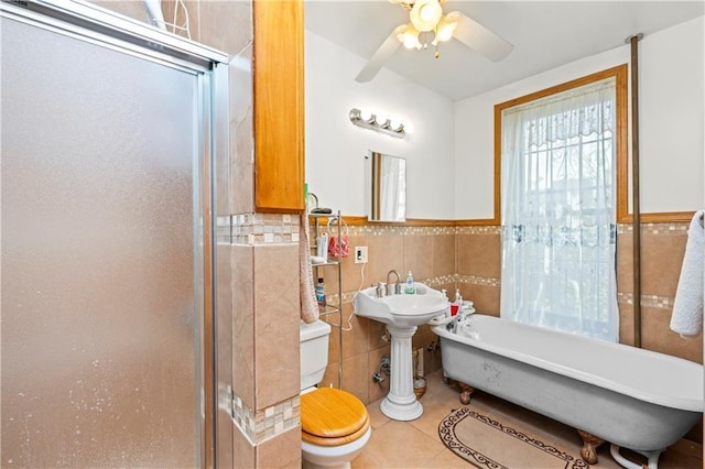 bathroom with tile walls, toilet, a ceiling fan, tile patterned floors, and a soaking tub
