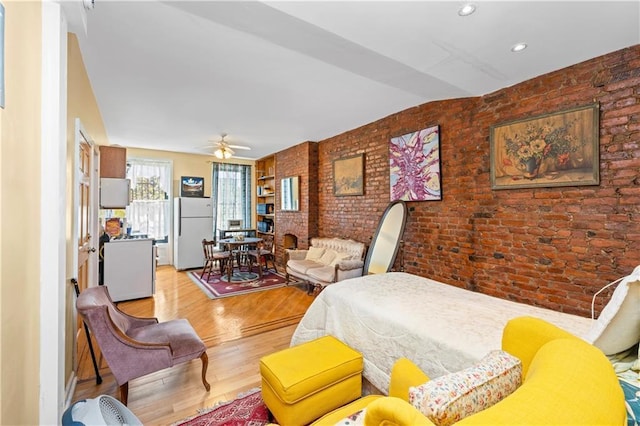 bedroom featuring freestanding refrigerator, brick wall, wood finished floors, and recessed lighting