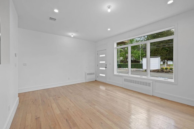 spare room with radiator, light wood finished floors, baseboards, and recessed lighting