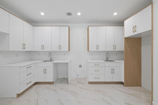 kitchen with a sink, light marble finish flooring, white cabinets, and recessed lighting