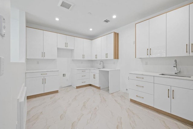 kitchen with a sink, light marble finish floors, recessed lighting, white cabinetry, and light countertops