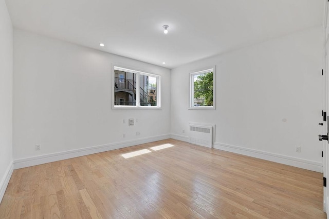 empty room with radiator heating unit, light wood finished floors, baseboards, and recessed lighting