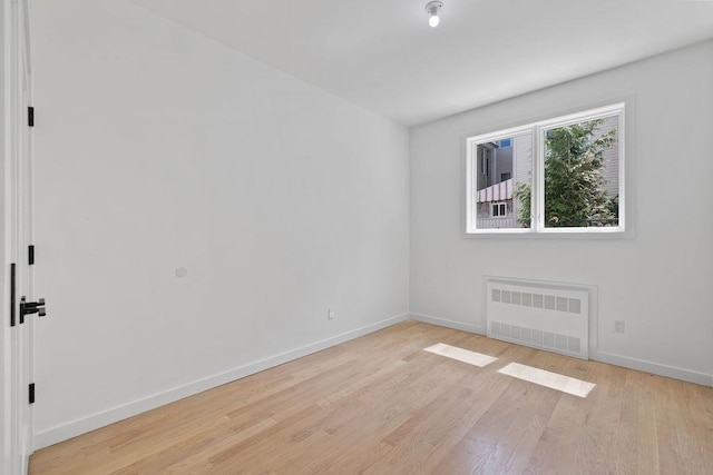 unfurnished room featuring radiator, light wood finished floors, and baseboards