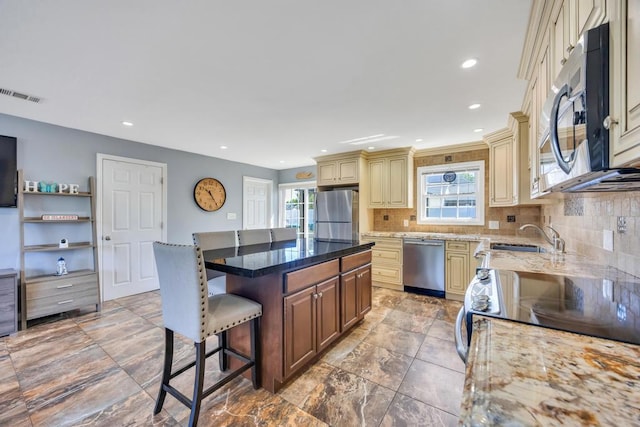59 Saddle Ln, Levittown, NY 11756 - kitchen featuring cream cabinets, stainless steel appliances, a sink, a kitchen bar, and plenty of natural light